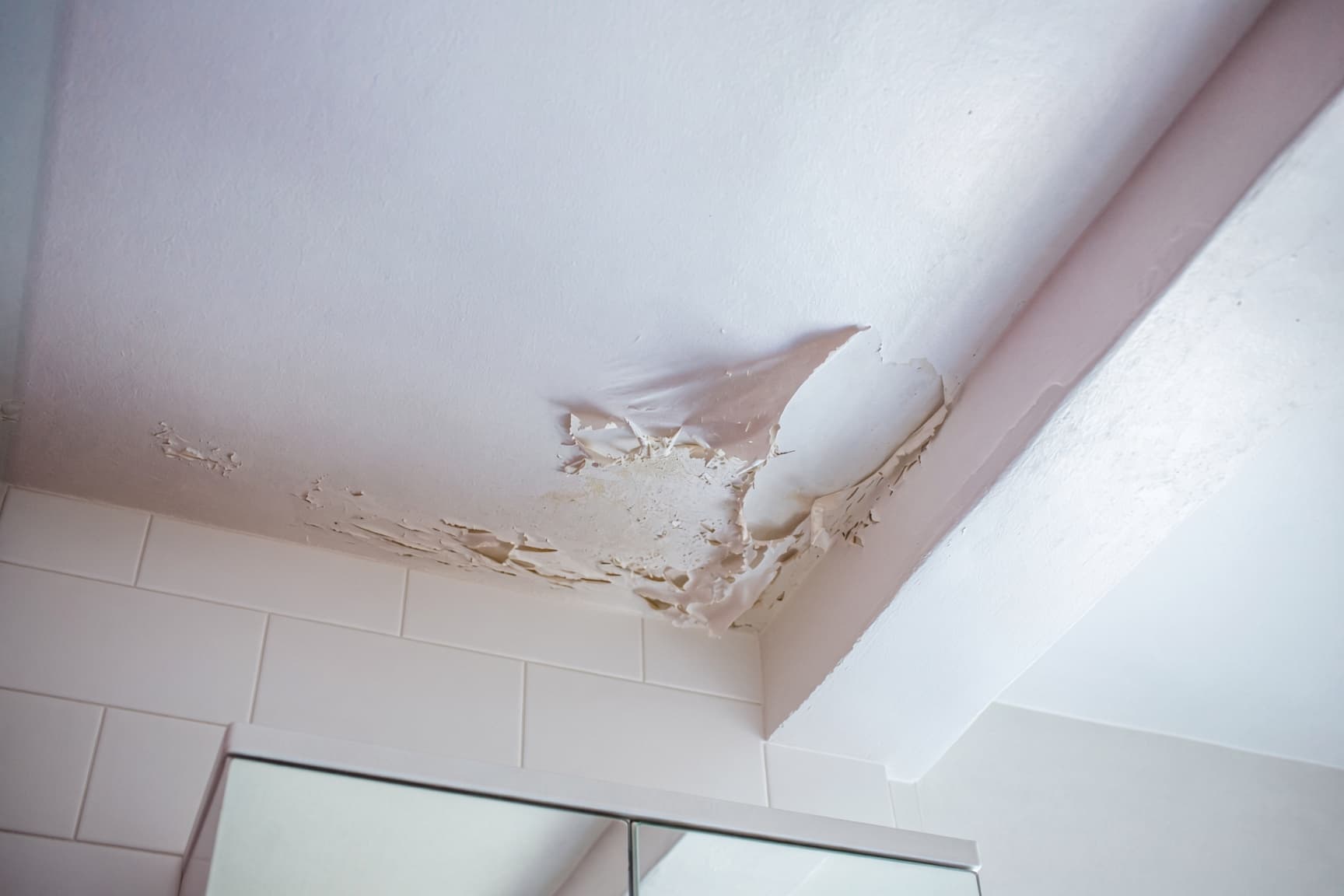 Peeling paint on a bathroom ceiling above a shower in a Raleigh home